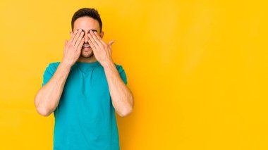 Sarı fırında izole edilmiş genç beyaz adam elleriyle gözlerini kapatıyor, geniş bir gülümsemeyle bir sürpriz bekliyor..