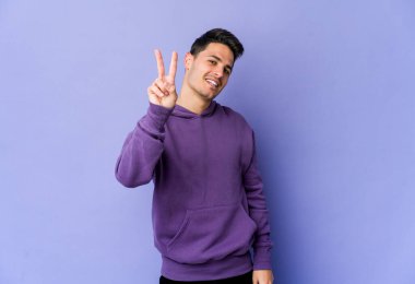 Mor arka planda izole edilmiş genç beyaz adam iki numarayı parmaklarıyla gösteriyor..