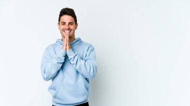 Beyaz arka planda izole edilmiş genç beyaz bir adam el ele tutuşup, ağız kenarında dua ediyor, kendinden emin..