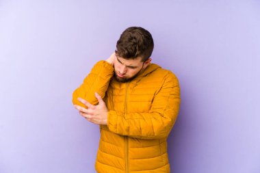 Genç beyaz adam mor arka planda izole edilmiş dirsek masajı yapıyor, kötü bir hareketin ardından acı çekiyor..