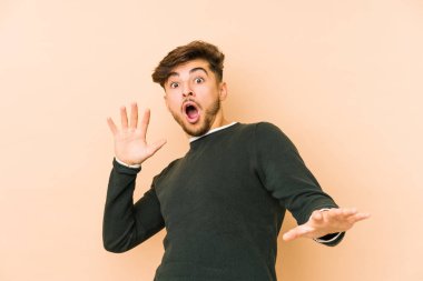 Genç Arap bir adam, yakın bir tehlike nedeniyle şok olan bej bir arka planda izole edildi.