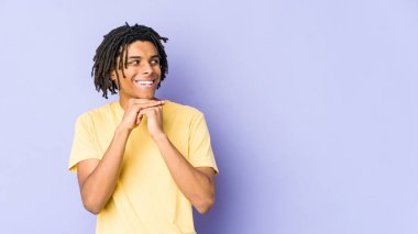 Genç Afrikalı Amerikalı Rasta adam ellerini çenesinin altında tutuyor ve mutlu bir şekilde yan tarafa bakıyor..