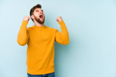 Mavi arka planda izole edilmiş genç beyaz bir adam zaferden sonra yumruğunu kaldırıyor, kazanan konsept..