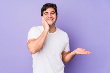 Mor arka planda izole edilmiş genç bir adam, bir avuç içinde fotokopi alanı tutar, el üstünde yanak tutar. Şaşırmış ve mutlu..