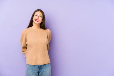 Mor arka planda izole edilmiş genç beyaz kadın gevşemiş ve mutlu bir şekilde gülüyor, boynunda dişlerini gösteriyor..