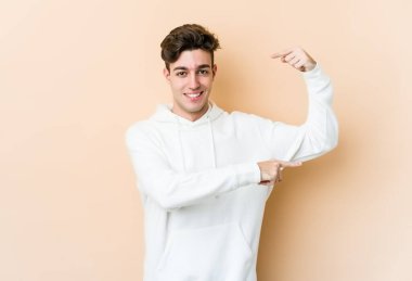 Beyaz tenli genç adam bej arka planda izole edilmiş. Elinde parmakları olan, gülümseyen ve kendinden emin bir şey var..