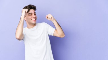 Mor arka planda izole genç beyaz adam özel bir günü kutluyor, atlıyor ve enerjiyle kollarını kaldırıyor..