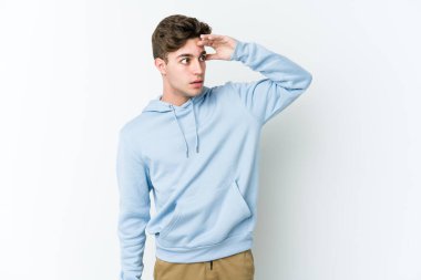 Beyaz arka planda izole edilmiş genç beyaz bir adam uzaklara bakıyor ve elini alnına koyuyor..