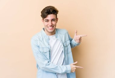 Beyaz tenli genç adam bej arka planda izole edilmiş ve işaret parmağıyla fotokopi alanını işaret ederek heyecan ve arzusunu ifade ediyor..