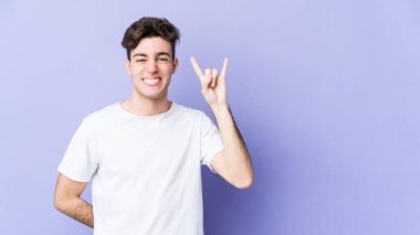 Mor arka planda izole edilmiş genç beyaz adam parmaklarıyla taş hareketi gösteriyor.