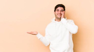 Bej arka planda izole edilmiş genç bir adam, bir avuç içinde fotokopi alanı tutuyor, el üstünde tutuyor. Şaşırmış ve mutlu..