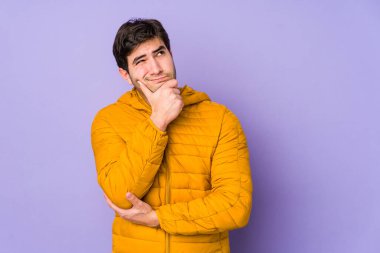 Genç adam mor arka planda izole edilmiş düşünüyor, yukarı bakıyor, yansıtıyor, düşünüyor, bir fantezi kuruyor..