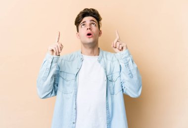 Beyazlı genç bir adam bej arka planda izole edilmiş. Ağzı açık, üst tarafı işaret ediyor..