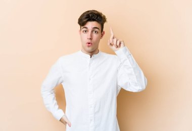 Beyazlı genç bir adam bej arka planda izole edilmiş. Ağzı açık, üst tarafı işaret ediyor..