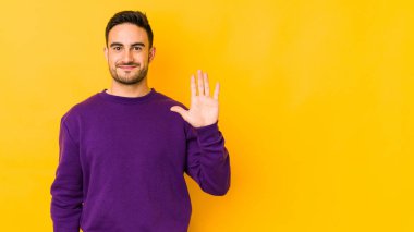 Sarı fırında izole edilmiş genç beyaz adam gülümseyerek beş numarayı parmaklarıyla gösteriyor..
