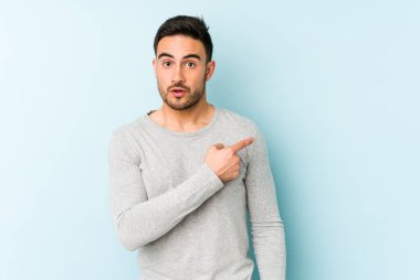 Mavi arka planda izole edilmiş genç beyaz adam gülümsüyor ve boş alanda bir şeyler gösteriyor..