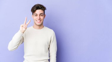 Mor arka planda izole edilmiş genç beyaz adam neşeli ve kaygısız parmakları olan bir barış sembolü gösteriyor..