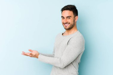 Mavi arka planda izole edilmiş genç beyaz bir adam palmiyesinde bir kopya alanı tutuyor..