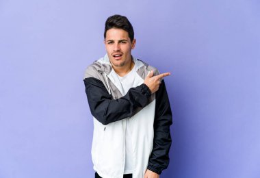 Mor arka planda izole edilmiş genç beyaz adam yan tarafı işaret ediyor.