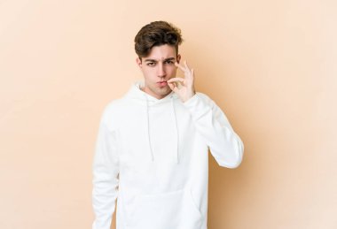 Beyazlı genç bir adam bej arka planda izole edilmiş ve parmakları dudaklarında bir sır saklıyor..