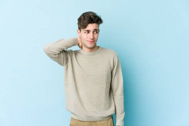 Kafkasyalı genç adam mavi arka planda izole edilmiş kafasının arkasına dokunuyor, düşünüyor ve bir seçim yapıyor..