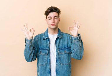 Beyaz tenli genç adam, bej arka planda izole edilmiş yoğun çalışma gününden sonra rahatlıyor, yoga yapıyor..