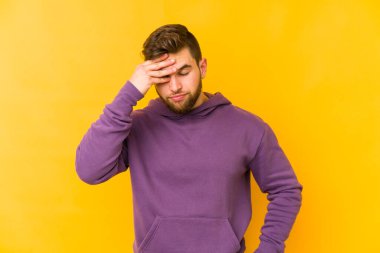 Kafkasyalı genç adam sarı arka planda izole edilmiş, başı ağrıyor, yüzüne dokunuyor..