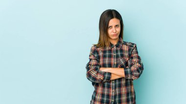 Mavi arka planda izole edilmiş genç bir kadın hoşnutsuzca kaşlarını çatmış, kollarını kavuşturmuş..