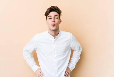 Beyazlı genç bir adam bej arka planda izole edilmiş komik ve dost canlısı bir dil kullanıyor..