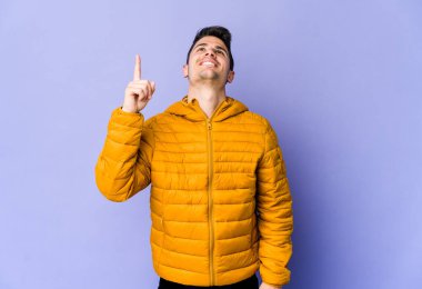 Mor arka planda izole genç beyaz adam iki ön parmağı da boş bir alan gösteriyor..