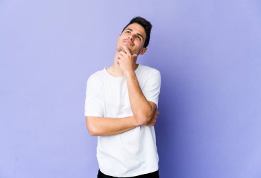 Mor arka planda izole edilmiş genç beyaz adam rahatlamış bir şeyin fotokopi odasına baktığını düşünüyor..