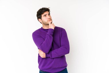 Beyaz arka planda izole edilmiş genç adam şüpheli ve şüpheci bir ifadeyle yana bakıyor..