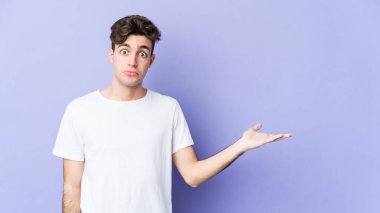 Mor arka planda izole edilmiş genç beyaz bir adam bir avuç içinde fotokopi alanı ve belinde bir el daha gösteriyor..