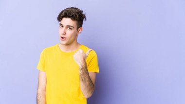 Mor arka plan noktalarında izole genç beyaz adam başparmak uzakta, gülüyor ve kaygısız.