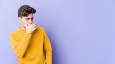 Mor arka planda izole edilmiş genç beyaz bir adam. Düşünceli bir şekilde ağzıyla ağzını kapatan bir fotokopi odasına bakıyor..