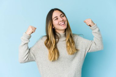 Genç beyaz kadın mavi arka planda izole edilmiş zafer sonrası yumruğunu kaldırıyor, kazanan konsept..