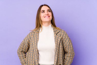 Mor arka planda izole edilmiş genç beyaz kadın gevşemiş ve mutlu bir şekilde gülüyor, boynunda dişlerini gösteriyor..