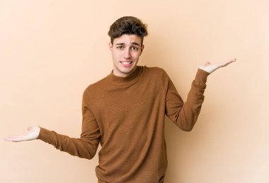 Kafkasyalı genç adam bej arka planda izole edilmiş. Kafası karışmış ve omuz silkiyor. Kopya alanını tutmak için..