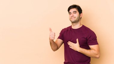 Bej arka planda izole edilmiş genç adam karnına dokunuyor, nazikçe gülümsüyor, yemek yiyor ve tatmin oluyor..