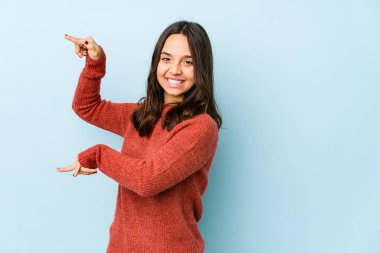 Genç, Latin kökenli bir kadın, kendini izole etmiş, parmaklarıyla küçük bir şey tutuyor, gülümsüyor ve kendinden emin..