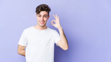 Mor arka planda izole edilmiş genç beyaz bir adam bir göz kırptı ve elleriyle iyi bir jest yaptı..
