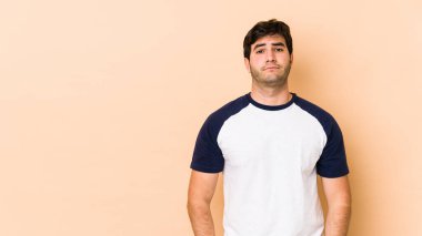 Bej arka planda izole edilmiş genç adam üzgün, ciddi yüzlü, mutsuz ve hoşnutsuz hissediyor..