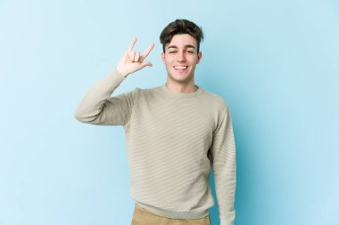 Mavi arka planda izole edilmiş genç beyaz adam boynuzlarını devrim konsepti olarak gösteriyor..