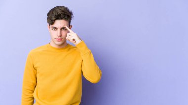 Mor arka planda izole edilmiş genç beyaz bir adam şakağı parmağıyla işaret ediyor, düşünüyor ve bir göreve odaklanıyor..