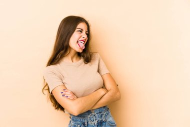 Beyaz tenli genç bir kadın bej arka planda izole edilmiş komik ve dost canlısı bir dil kullanıyor..