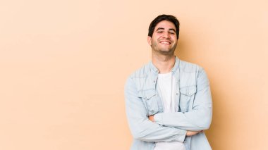 Bej arka planda izole genç bir adam kendinden emin, kararlılıkla kollarını kavuşturuyor..