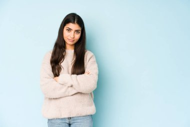 Mavi arka planda izole edilmiş genç Hintli kadın sıkılmış, yorgun ve dinlenmeye ihtiyacı var..