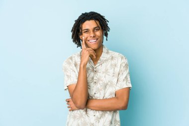 Genç Afrikalı Amerikalı Rasta adam mutlu ve kendinden emin gülümsüyor, elleriyle çenesine dokunuyor..