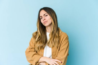 Mavi arka planda izole edilmiş genç beyaz kadın alaycı bir ifadeyle kameraya bakarken mutsuz oluyor..