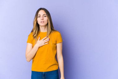 Mor arka planda izole edilmiş genç beyaz kadın yemin ediyor, elini göğsüne koyuyor..